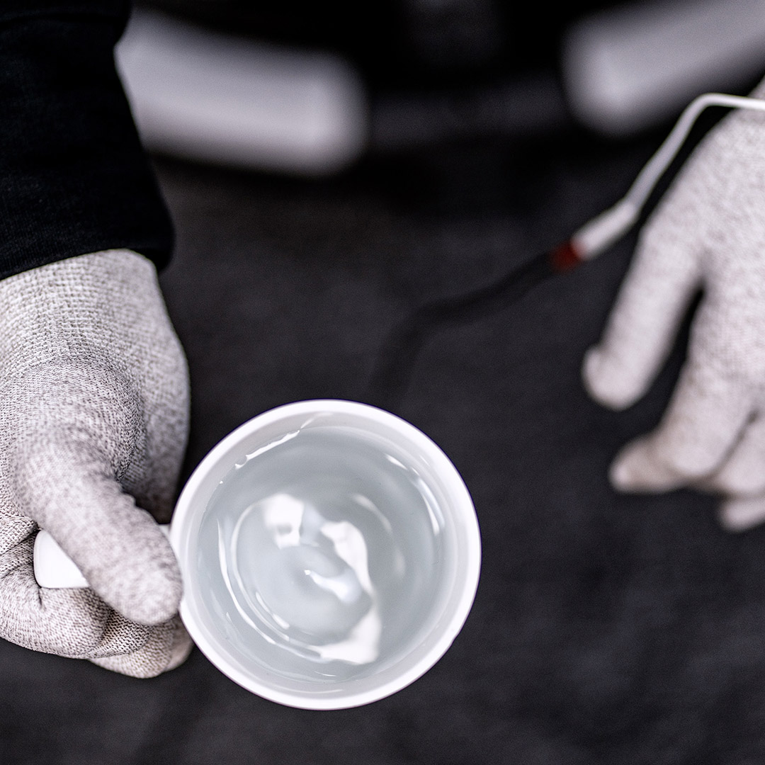 Top view photo of a hand wearing Parkinson's disease imitating gloves, holding a cup of water in the right hand - the surface of the water is clearly weaved due to hand shake.